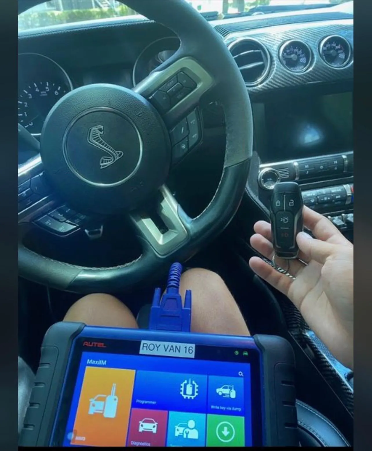 A person holds a remote control in front of a car, demonstrating car key transponder reprogramming.