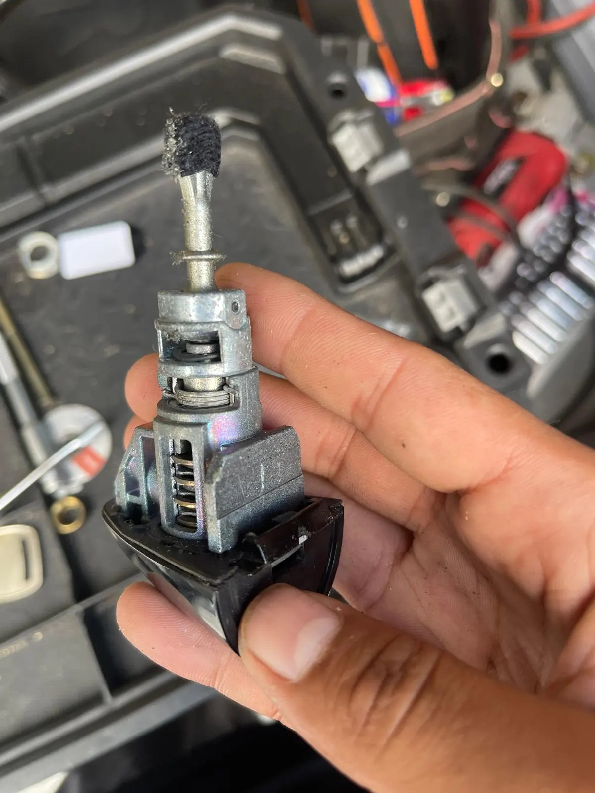 A person holding a small device, possibly for car lock rekeying, in their hand.