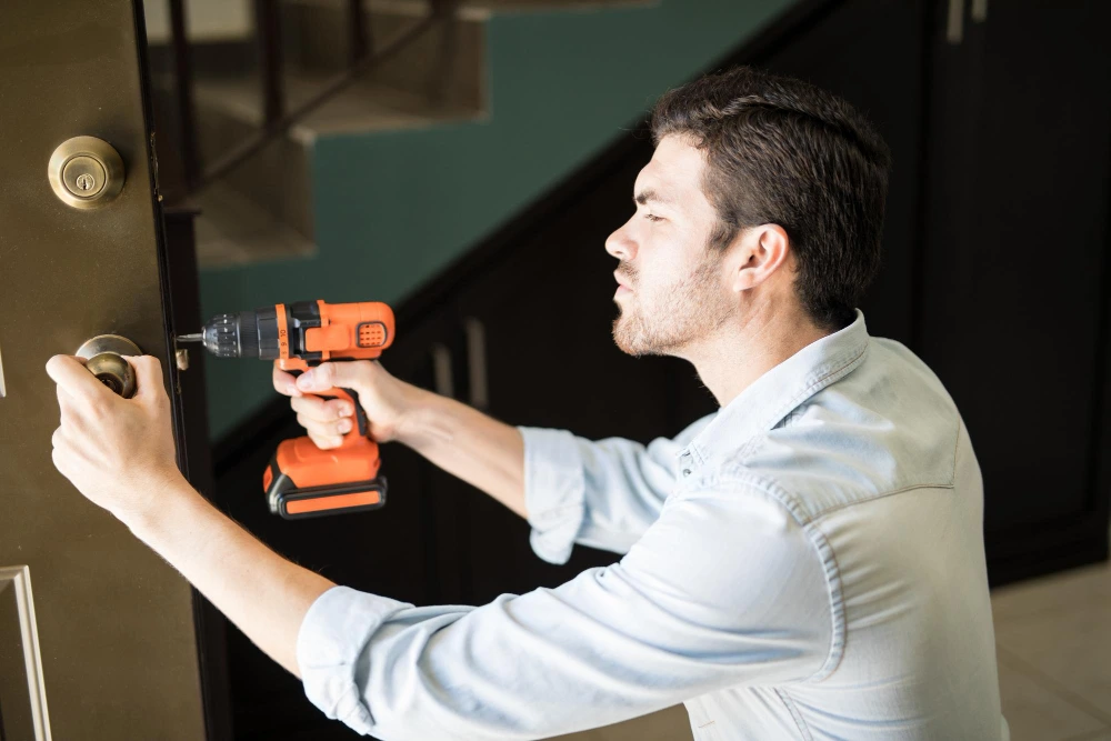 A man operates a drill to unlock a door as part of commercial lock repair.