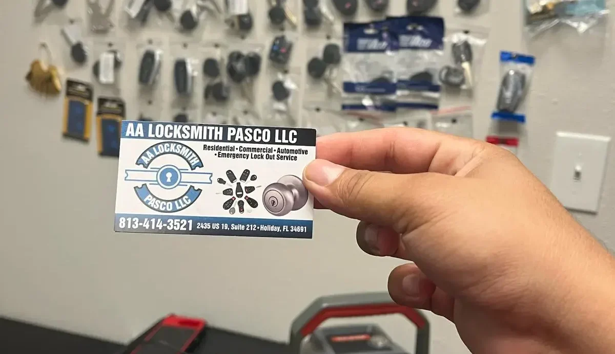 A person holds a business card for a locksmith service in front of a wall filled with various tools.
