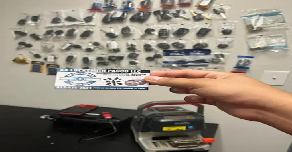 and holding an AA Locksmith Pasco LLC business card inside a locksmith workshop, with tools and replacement keys in the background—highlighting the modern services and options available to consumers in 2025.