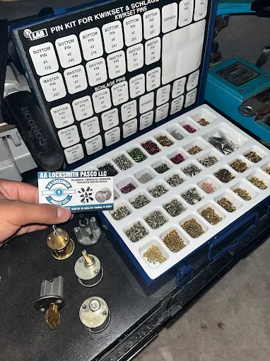 A locksmith from AA Locksmith Pasco LLC holding a business card beside a lock pinning kit and rekeyed cylinders, representing expert lock rekeying service.