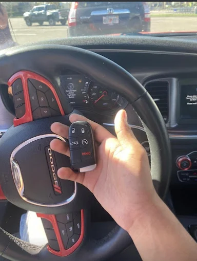 A locksmith from AA Locksmith Pasco LLC holding a car key fob inside a vehicle, representing professional ignition repair service.