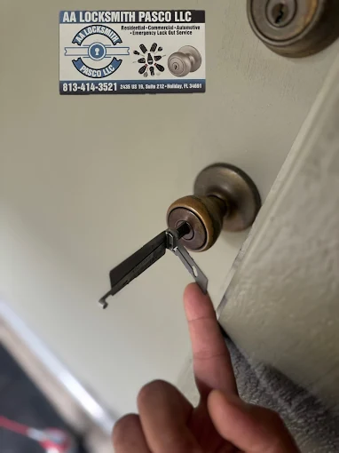 A person pointing at a key inserted into a door lock while holding an AA Locksmith Pasco LLC business card, representing professional residential locksmith services.