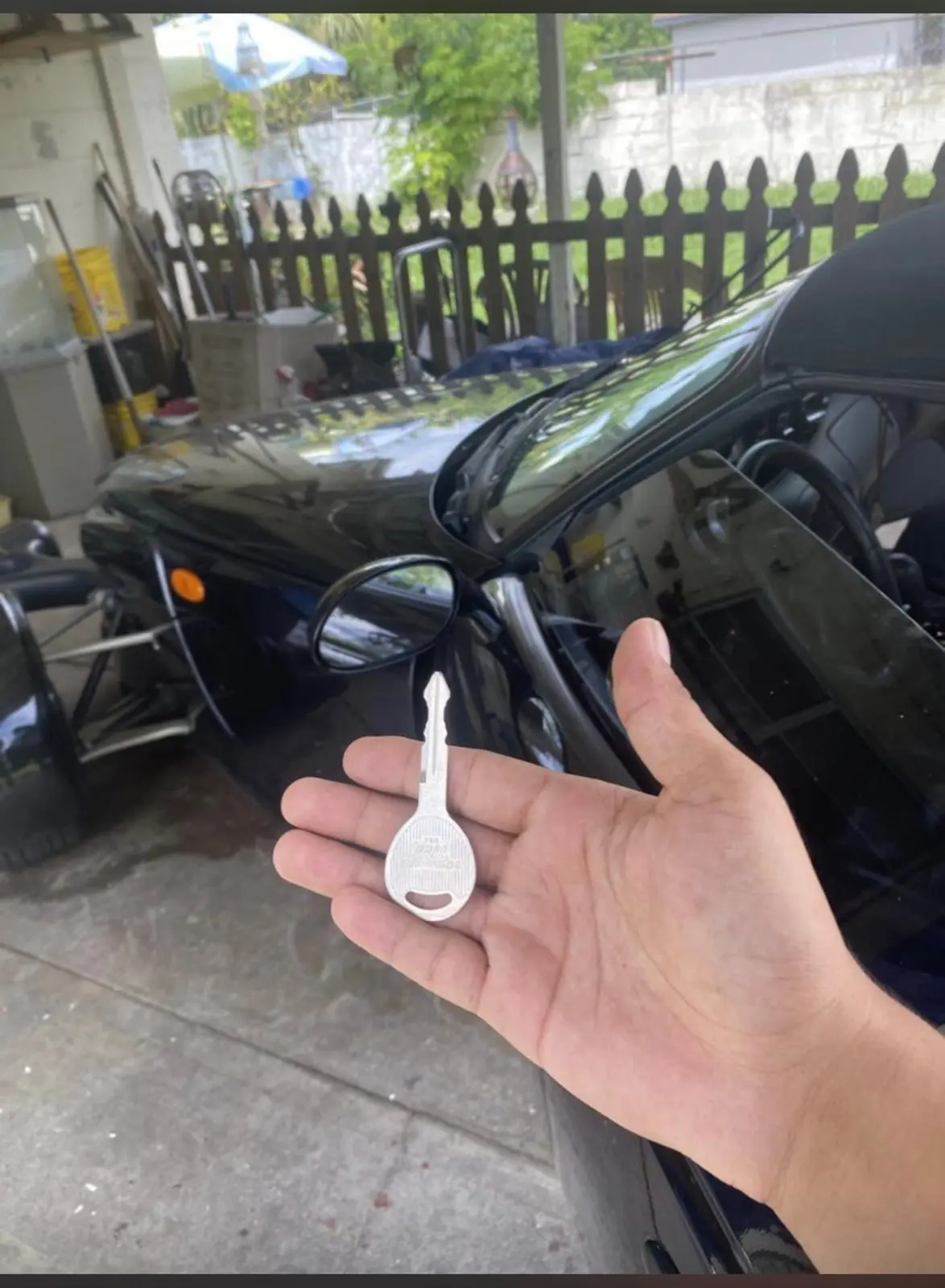 A locksmith from AA Locksmith Pasco LLC holding a newly cut car key beside a black vehicle, representing professional broken key extraction service.