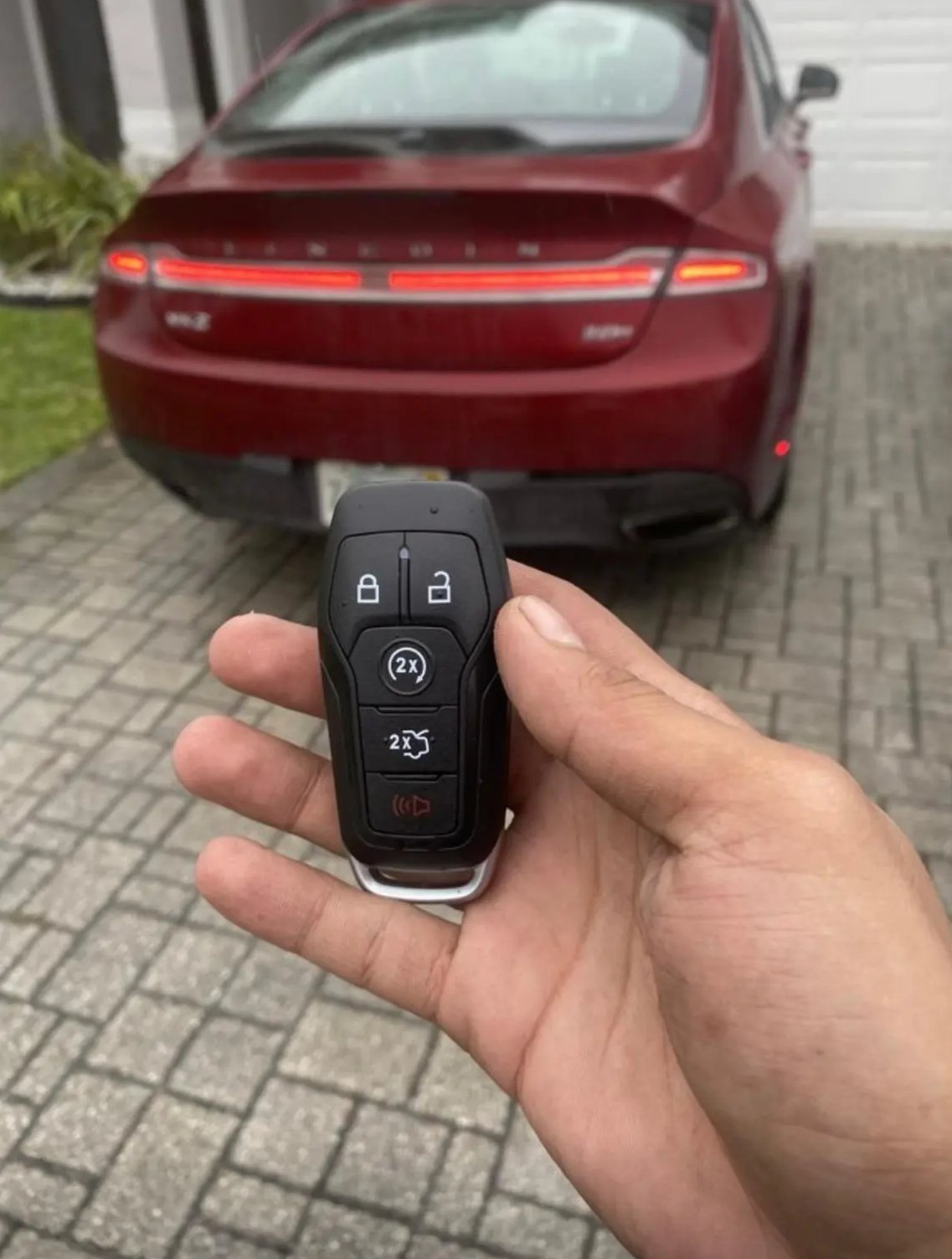 A locksmith from AA Locksmith Pasco LLC holding a modern car key fob near a red vehicle, representing expert car key replacement service.