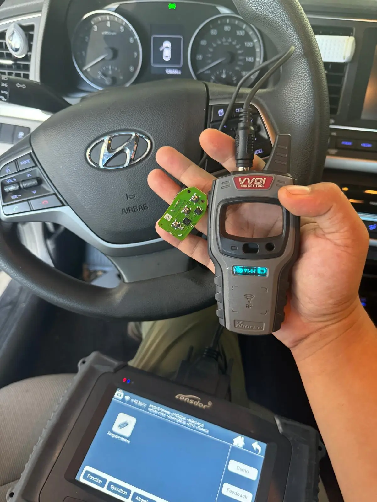 A locksmith from AA Locksmith Pasco LLC using diagnostic tools and holding a car key circuit board inside a vehicle, representing professional ignition replacement service.