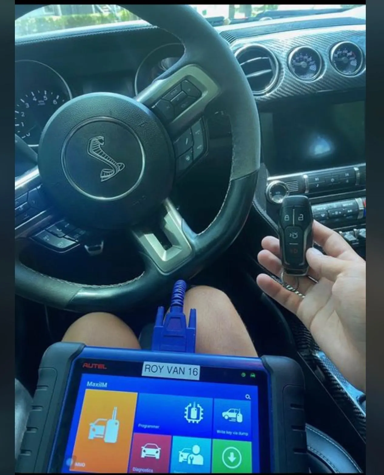 A locksmith from AA Locksmith Pasco LLC using a diagnostic tool and holding a car key fob inside a vehicle, representing expert ignition repair service.